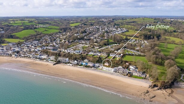 Vista aérea de un pueblo costero con playa, casas y una Ruby Cottage señalizada.