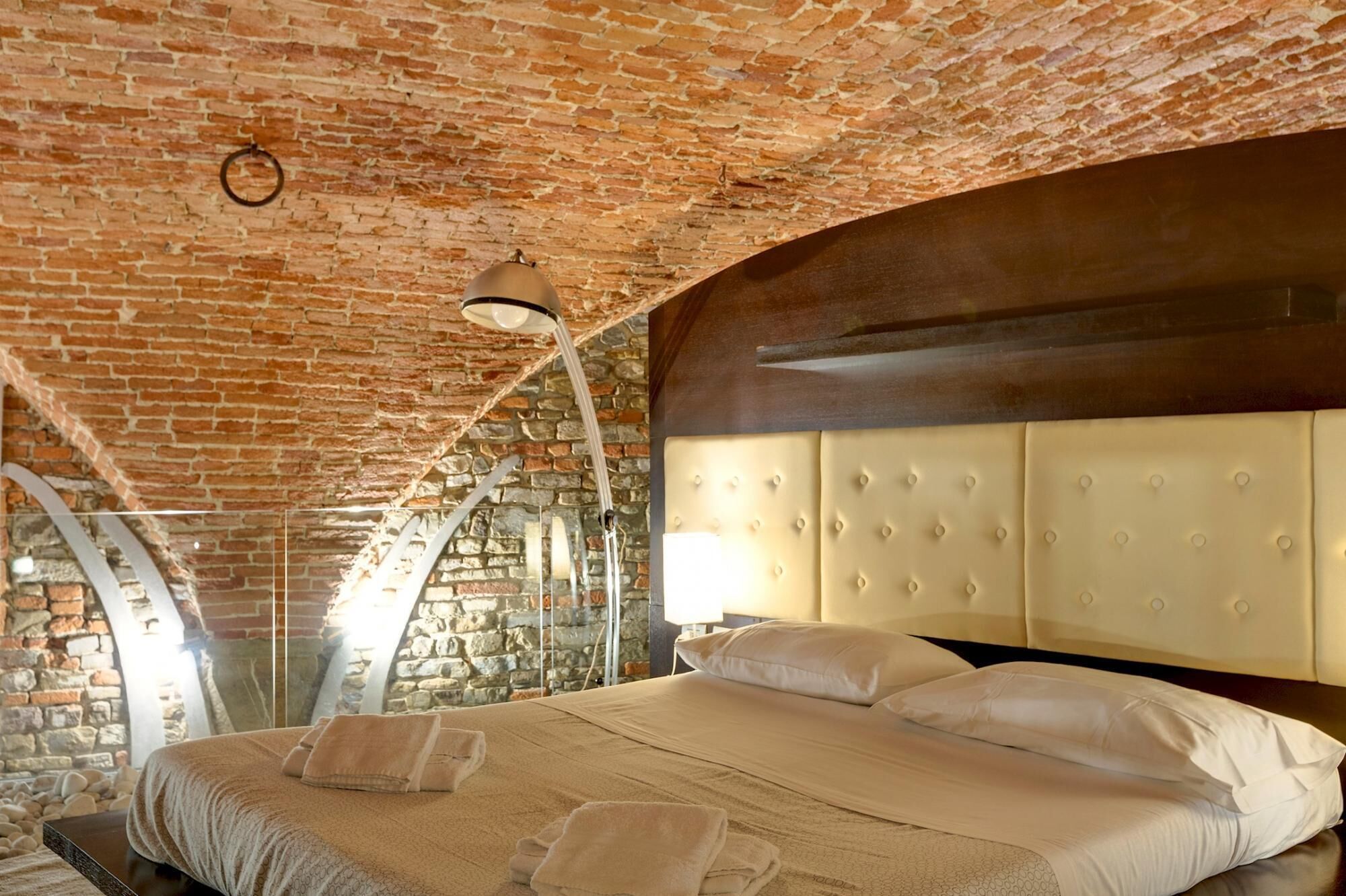Une chambre avec un plafond en briques, un grand lit doté d’une tête de lit capitonnée et un mur en pierre.