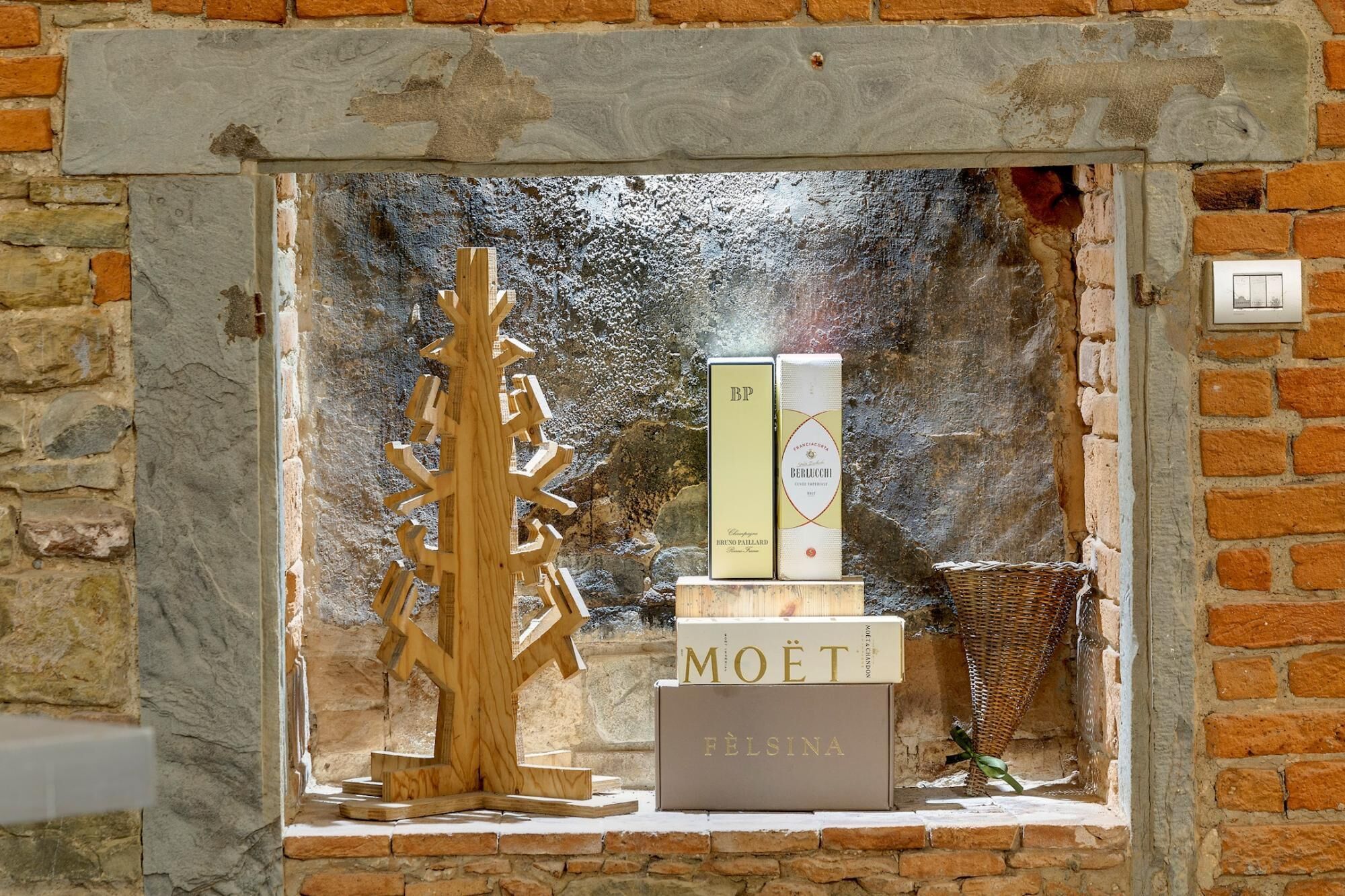 A display of wine bottles in a stone-walled alcove with a wooden sculpture.