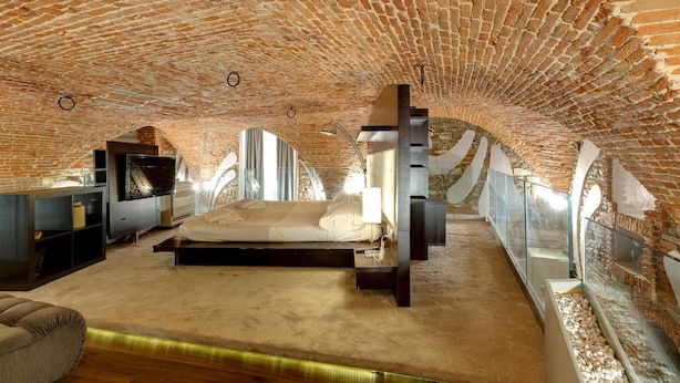 Une chambre mansardée avec de hauts plafonds, des murs en briques apparentes, un grand lit et une cheminée.