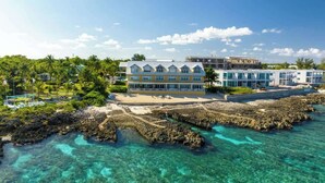 Un hôtel situé en bord de mer, composé de plusieurs bâtiments, avec une eau turquoise cristalline et des formations rocheuses.