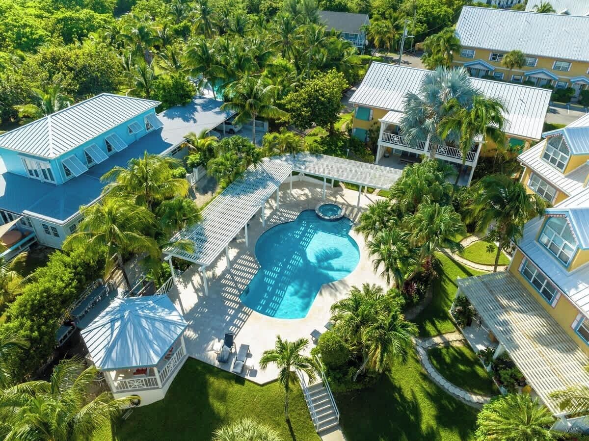 An aerial view of a residential area with a large swimming pool surrounded by lush greenery and multiple houses with blue roofs.