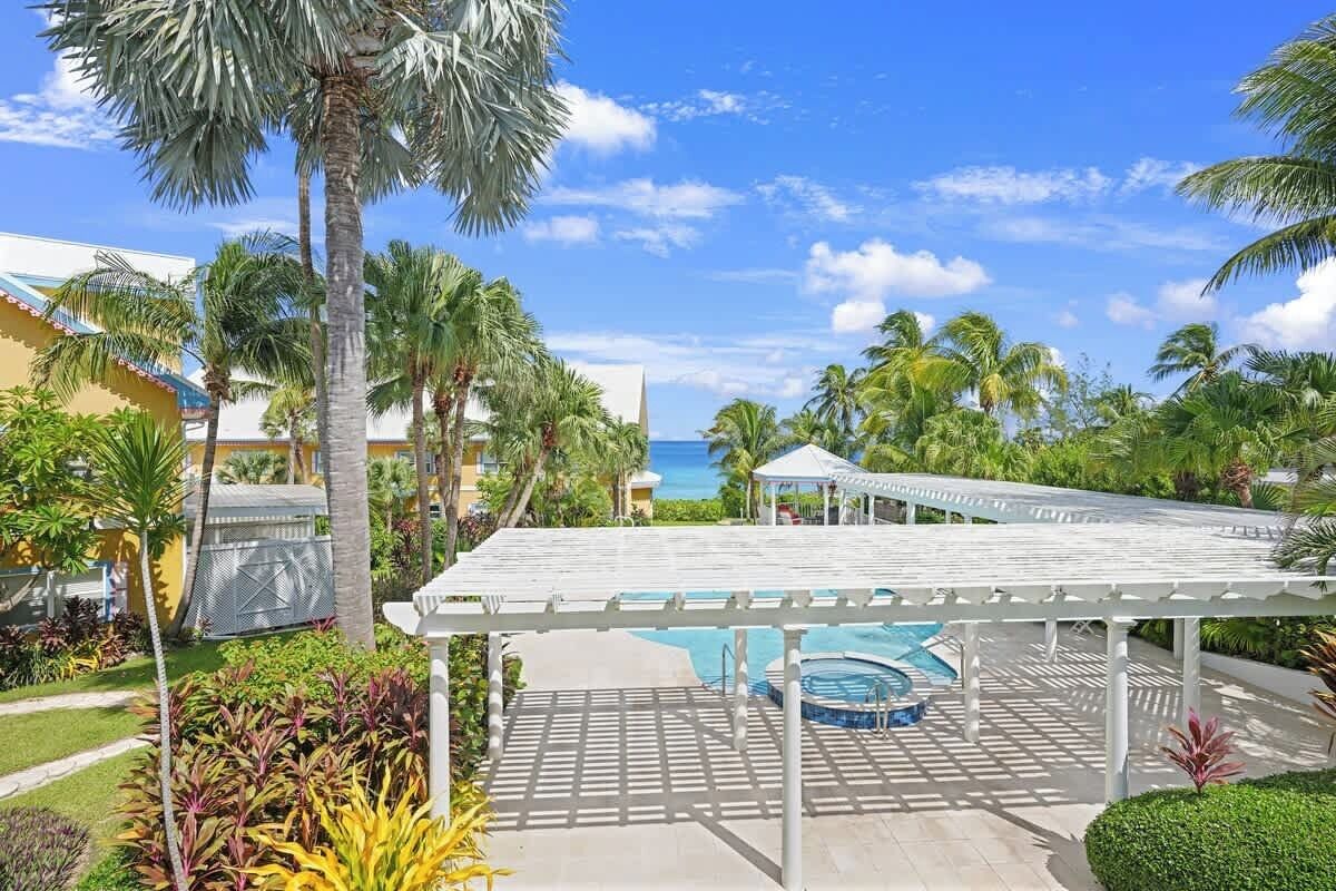 Een zwembadgedeelte van een resort met een overdekte pergola, palmbomen en uitzicht op de oceaan.