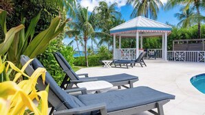 Un espace aménagé au bord de la piscine, avec des chaises longues, un kiosque et une vue sur l’océan.