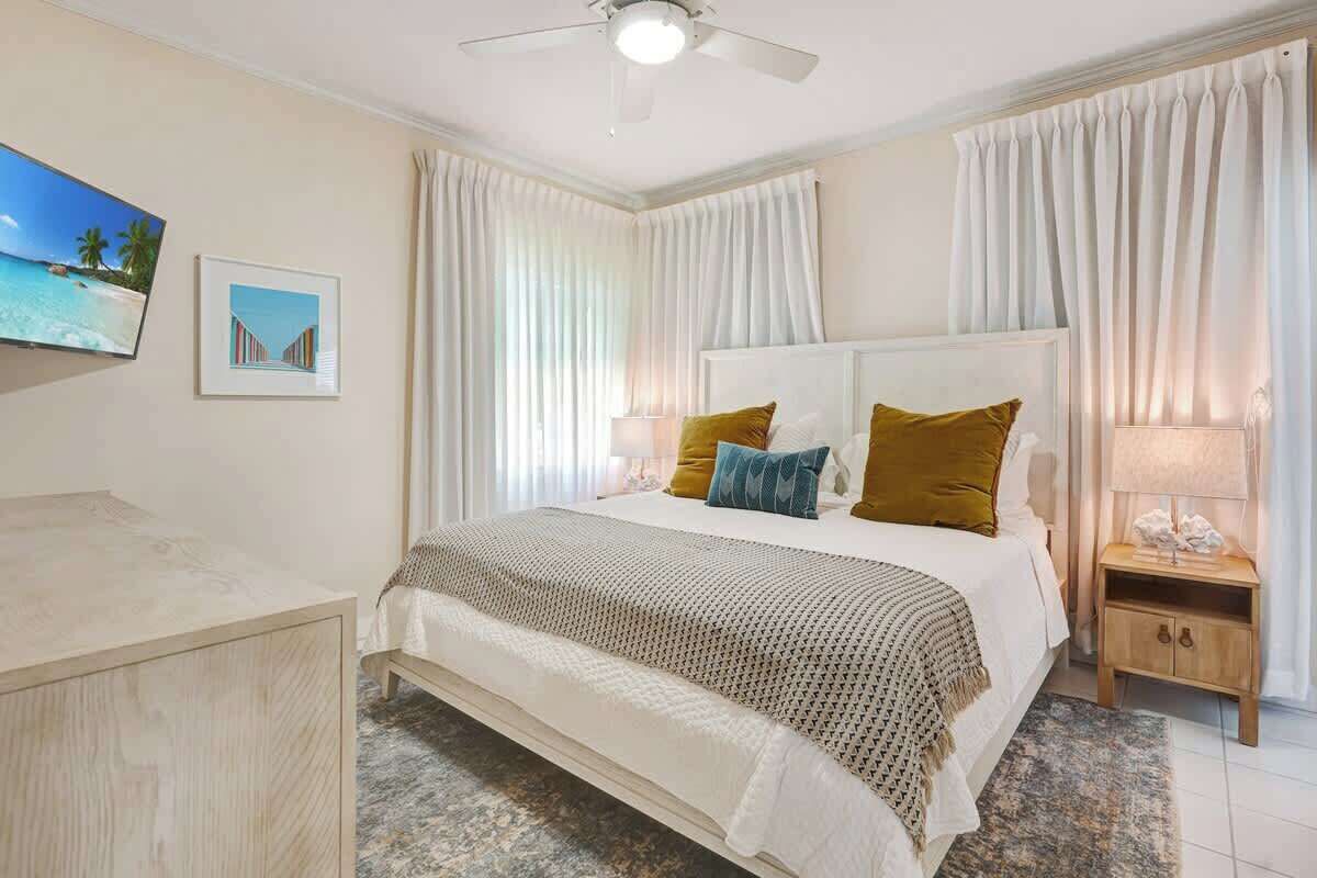 A hotel room with a bed, a nightstand, a ceiling fan, and a TV on the wall.