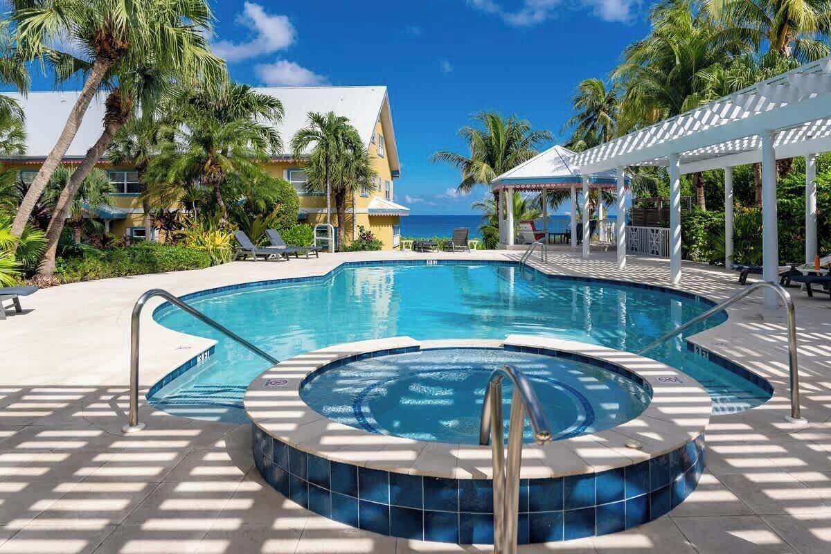A pool area with a hot tub, lounge chairs, and a view of the ocean.