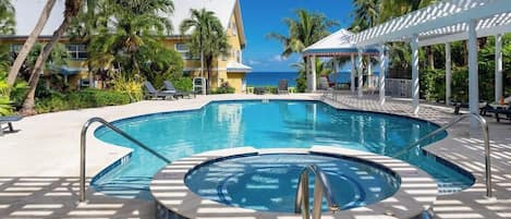 A pool area with a hot tub, lounge chairs, and a view of the ocean.