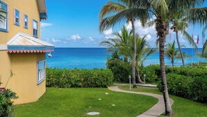 A yellow building with a small attached structure, a pathway leading to the ocean, and palm trees.