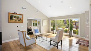 A spacious living room with a large window, a dining area, and a view of a garden. - Huge Secluded Cowan Heights Home, Pool, Entertainers Delight (4 beds/5 baths) (Santa Ana)