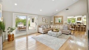 A spacious living room with a large sofa, a coffee table, and a dining area with chairs. There is a sliding glass door leading to an outdoor patio. - Huge Secluded Cowan Heights Home, Pool, Entertainers Delight (4 beds/5 baths) (Santa Ana)