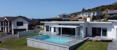 Una moderna casa a due piani con una grande area piscina vetrata e un patio coperto.