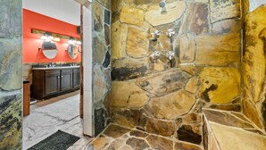 Ein Badezimmer mit einer Steinwand, einem Waschbecken mit Spiegel und einer Duschkabine.