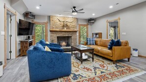 Ein modernes Wohnzimmer mit Kamin aus Stein, blauen Sofas, einem gemusterten Teppich und einem an der Wand befestigten Fernseher.