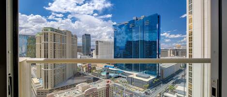 A cityscape through a window with high-rise buildings, including a prominent glass skyscraper.