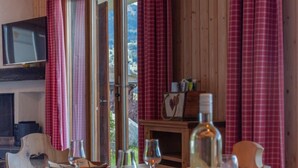 Een eethoek met een houten tafel gedekt voor twee personen, een aan de muur bevestigde televisie en een uitzicht op het landschap door grote ramen met rode gordijnen.