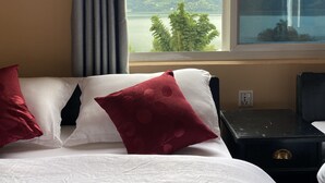Habitación de hotel con cama, mesita de noche y ventana con vista a una montaña y un lago.