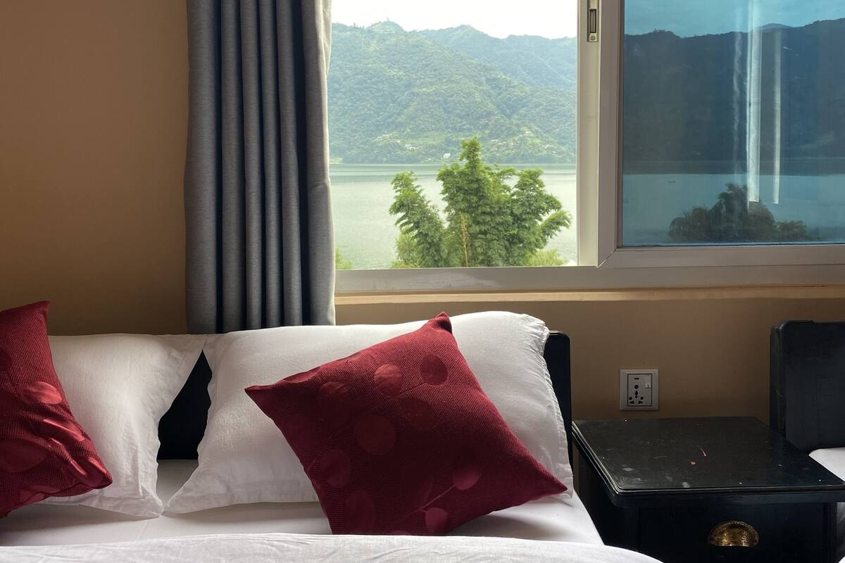 Habitación de hotel con cama, mesita de noche y ventana con vista a una montaña y un lago.