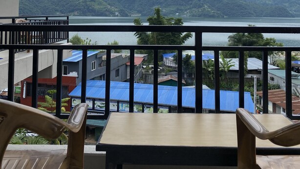 A balcony with a table and chairs, overlooking a mountainous landscape and a body of water. - The eagle Zone (Pokhara)