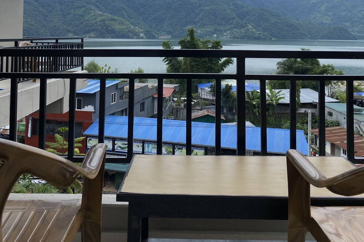 Un balcón con una mesa y sillas, con vistas a un paisaje montañoso y una masa de agua.