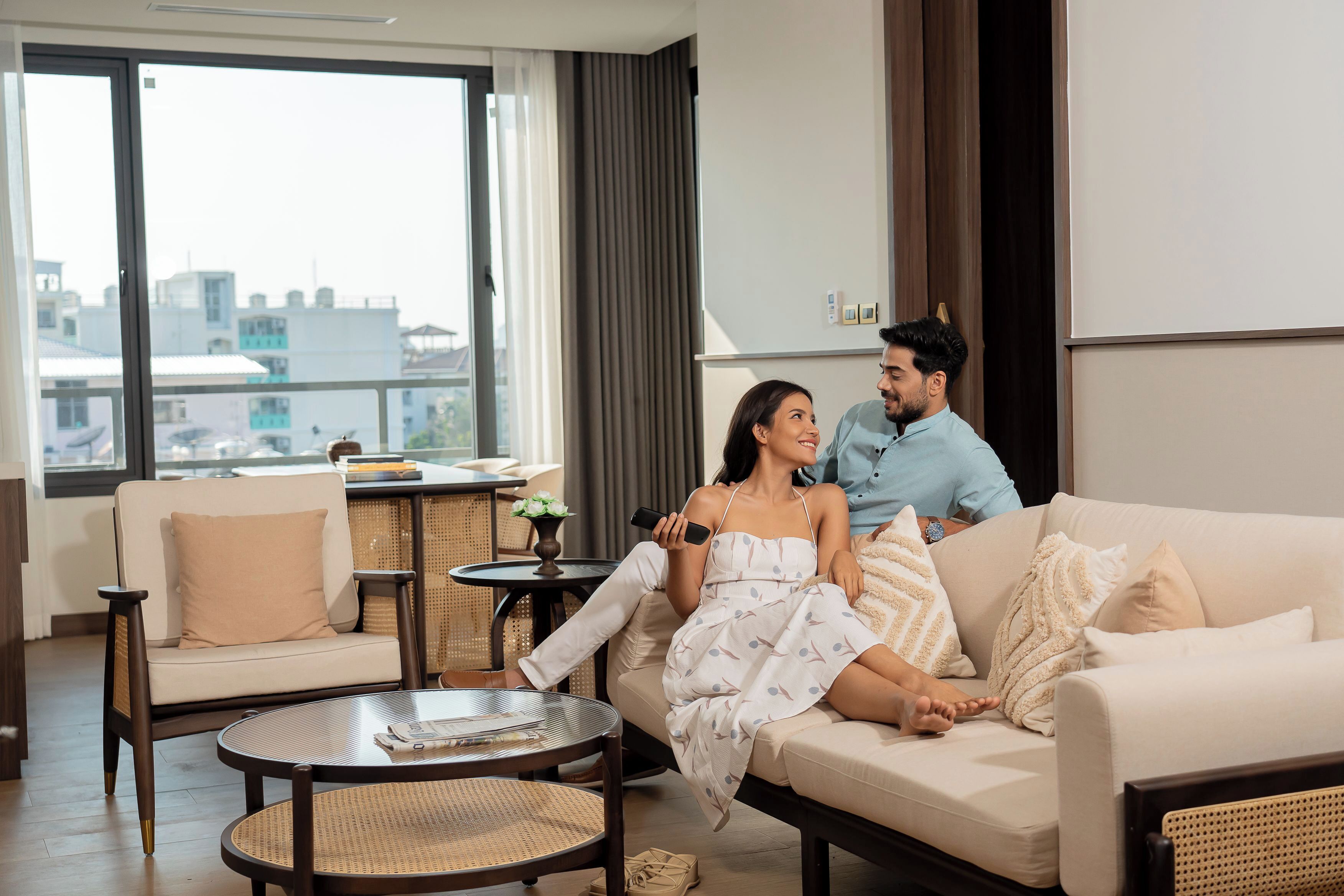 A modern living room with a sofa, a round coffee table, and a view of the city through large windows.