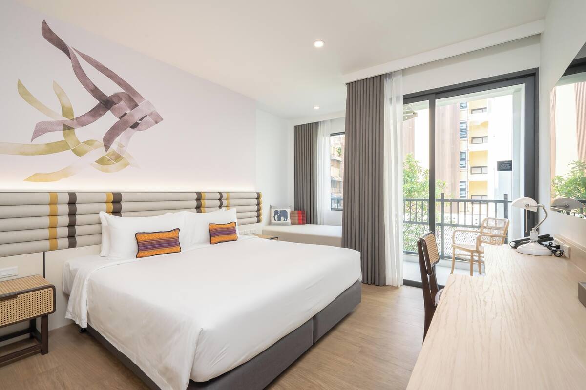 Habitació d'hotel moderna amb un llit gran, un escriptori i un balcó amb vista a la ciutat.