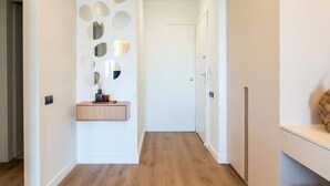 A hallway with a wooden floor, a white wall with circular mirrors, and a wooden bench. - 2-BD Luxury Apt  Sea View Balcony near the beach (Voula)