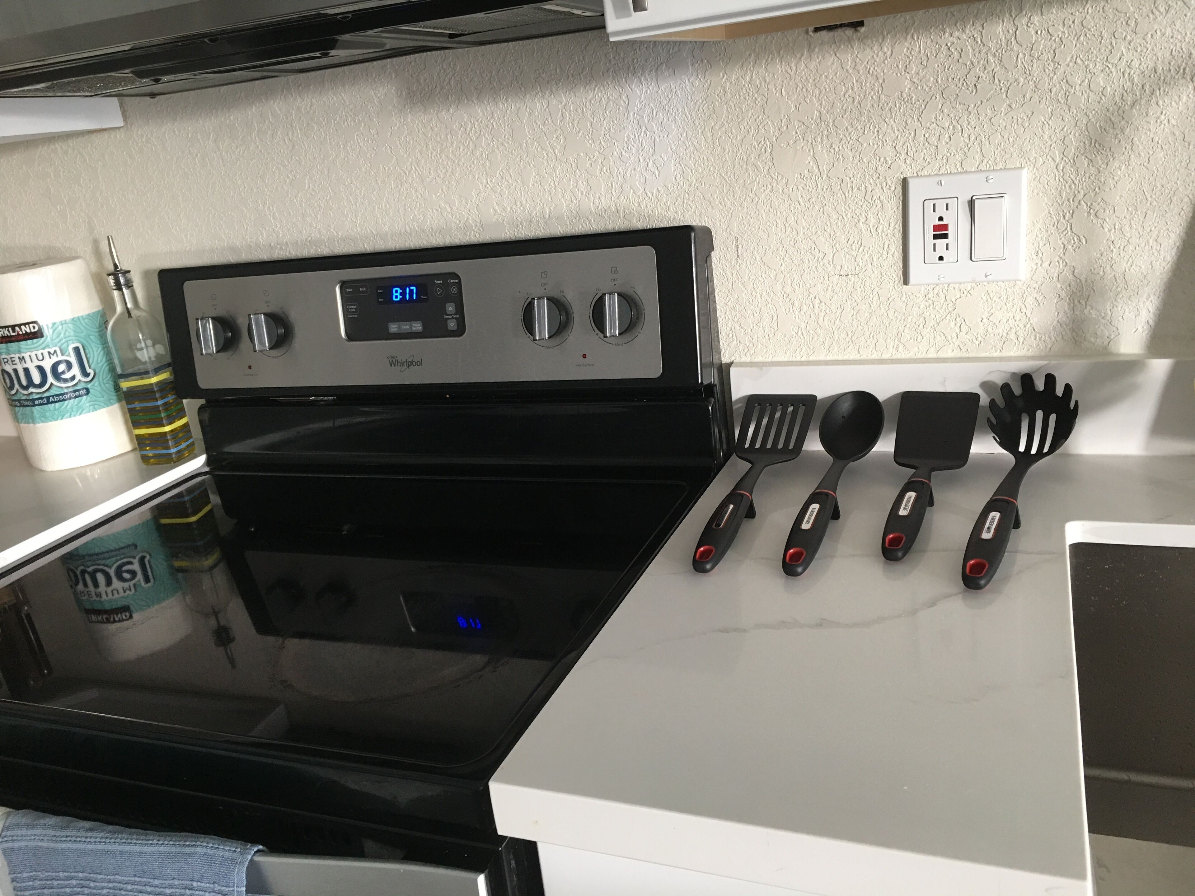 Et køkken med en sort Whirlpool komfur, en hvid bordplade og diverse køkkenredskaber.