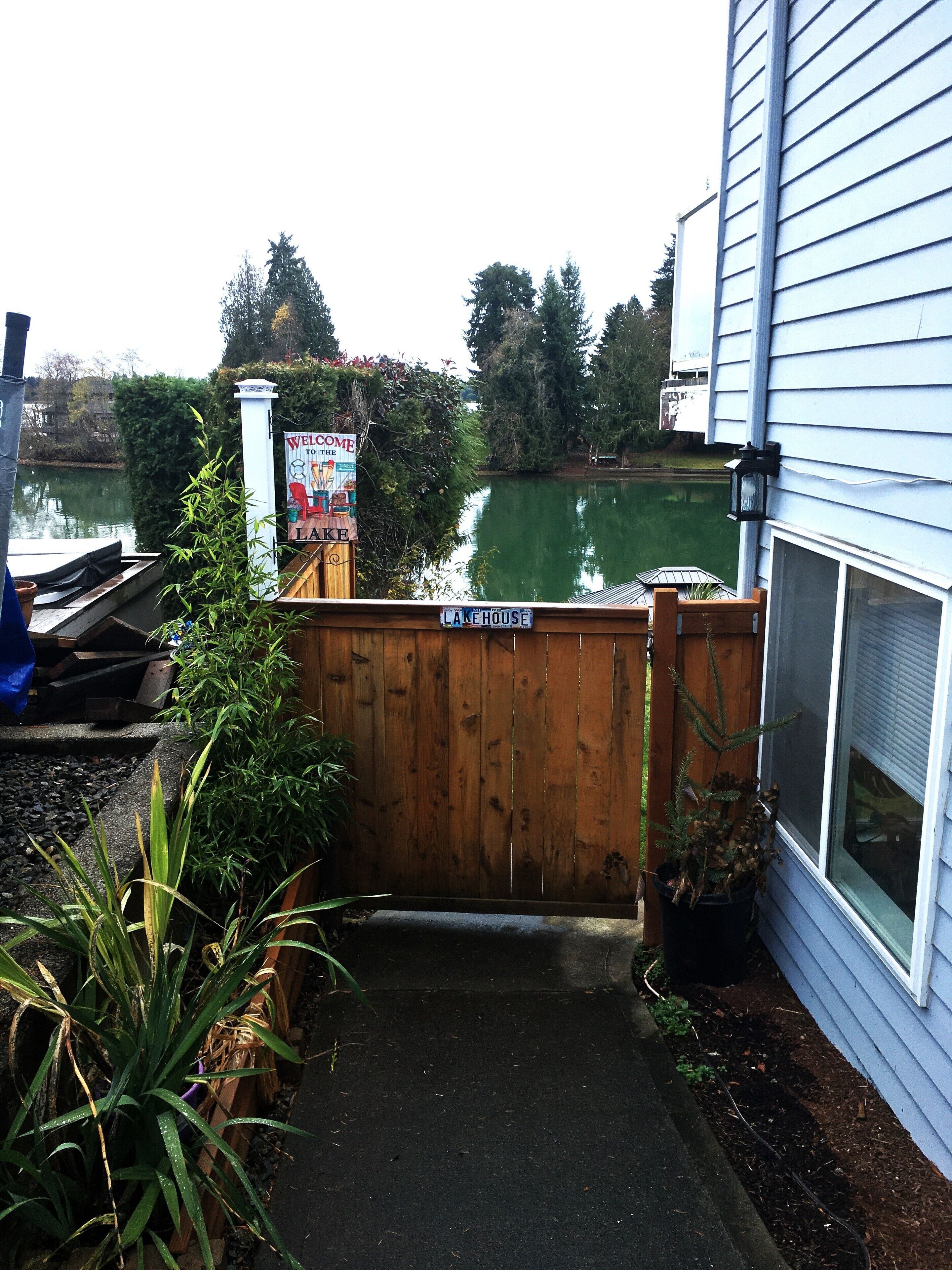 A wooden gate leading to a dock with a sign reading "Welcome to the Lake House."