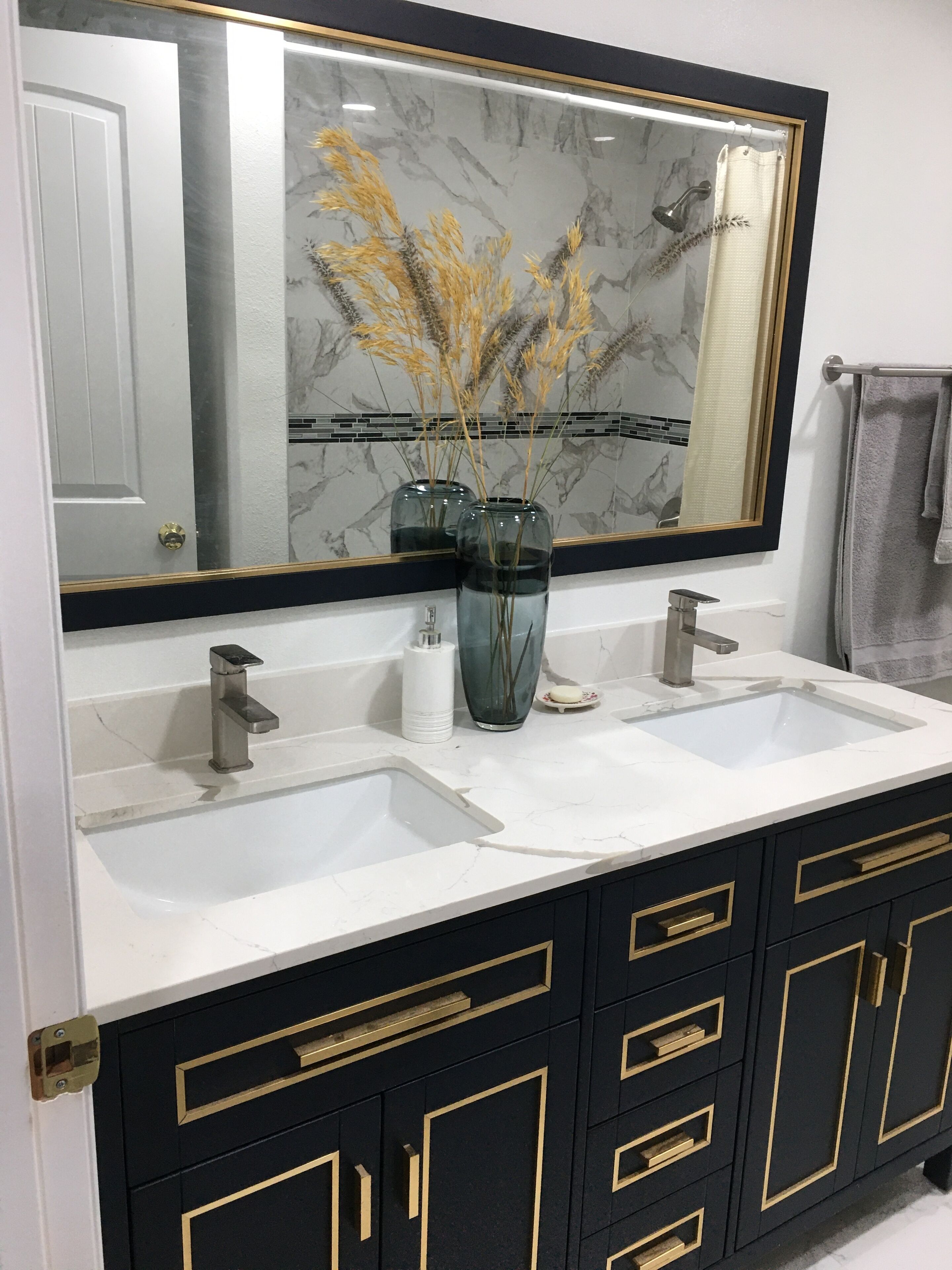 A bathroom with a double sink, a large mirror, and black cabinets with gold handles.