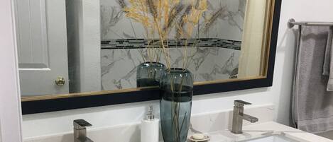 A bathroom with a double sink, a large mirror, and black cabinets with gold handles.