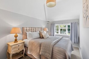 A bedroom with a large bed, two bedside tables, and a window with curtains.