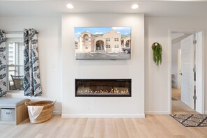 A modern living room with a fireplace, a mounted TV displaying a building, and a basket on the floor.
