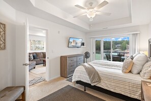 A bedroom with a bed, a dresser, a television, and a view of the outdoors.