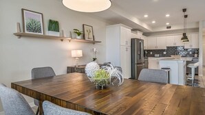 A modern kitchen with white cabinets, a central island, and a dining area with a wooden table and gray chairs. - Superb, Spacious Condo, Prime Resort! (Kissimmee)