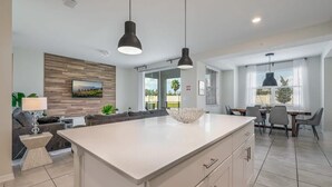A modern kitchen with a large island, pendant lighting, and a dining area with a table and chairs. - Superb, Spacious Condo, Prime Resort! (Kissimmee)