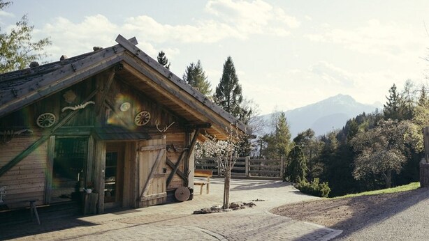 A rustic wooden building with a sloped roof, a wooden door, and a window with a circular design. - Holiday Apartment "Obertimpflerhof Lola" with Mountain View, Private Terrace & Wi-Fi (Verano)