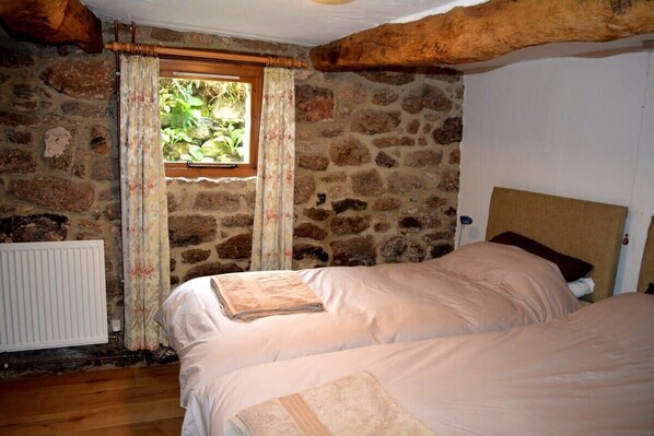 A bedroom with stone walls, a wooden ceiling, a window with curtains, and two beds with pillows. - Idyllic Dartmoor Cottage (Postbridge)