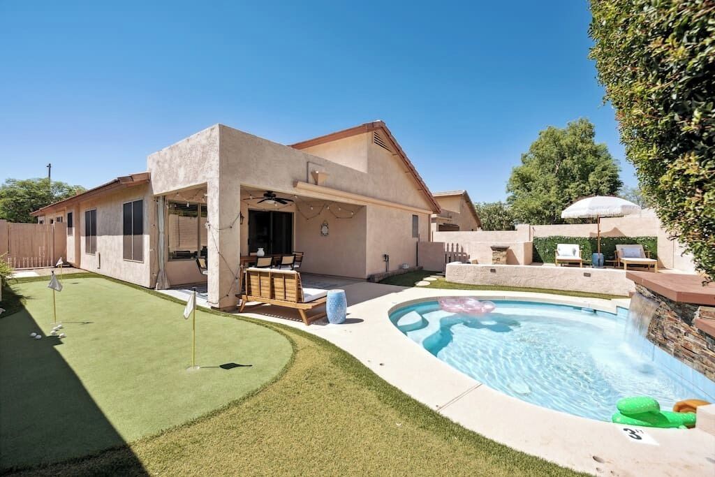 A modern house with a swimming pool, a patio with outdoor furniture, and a well-maintained lawn.