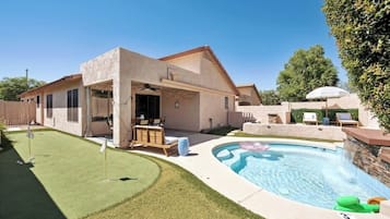 Una casa moderna con piscina, un patio con mobiliario exterior y un césped bien cuidado.