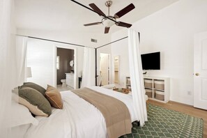 A bedroom with a bed, a ceiling fan, a TV, a wardrobe, and a mirror.