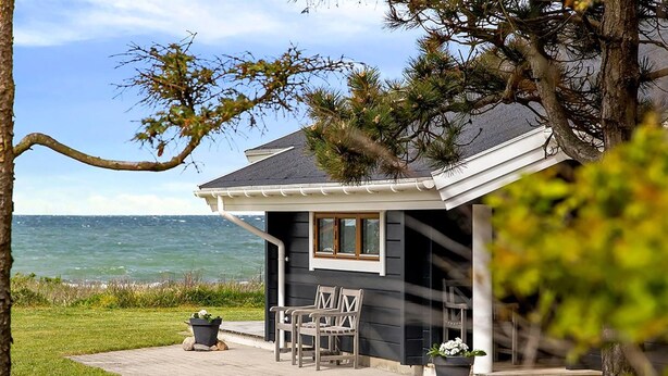 Une maison située sur la côte, dotée d’un patio, de deux chaises et d’une plante en pot.