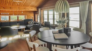 Un intérieur moderne avec une table ronde, des chaises blanches et un canapé. On y trouve des fenêtres avec des rideaux, un plafond en bois et une plante sur la table.