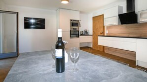 A modern kitchen with white cabinets, a wooden countertop, and a wine bottle on the table. - Der Pinsler by Interhome (Fügen)