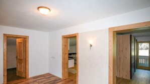 A spacious room with wooden flooring, white walls, and a ceiling light. There are wooden doors leading to other rooms. - Der Pinsler by Interhome (Fügen)