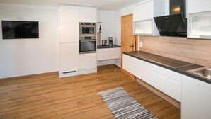 A modern kitchen with white cabinets, a built-in oven, a microwave, and a black range hood. - Der Pinsler by Interhome (Fügen)
