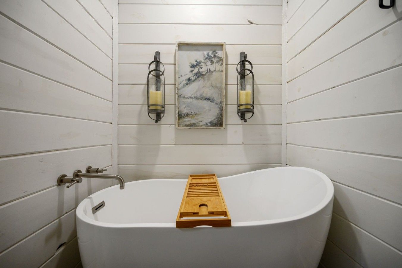 Een badkamer met een vrijstaand bad, een houten badmat en twee wandlampen.