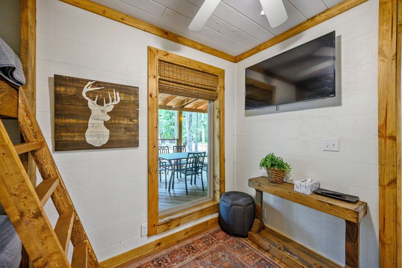 Una habitación con una escalera de madera, un televisor montado, una obra de arte con cabeza de venado enmarcadas y una puerta que da a una zona de estar exterior.