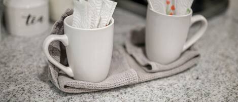 Two white ceramic mugs on a speckled countertop, each with a napkin holder containing a napkin.
