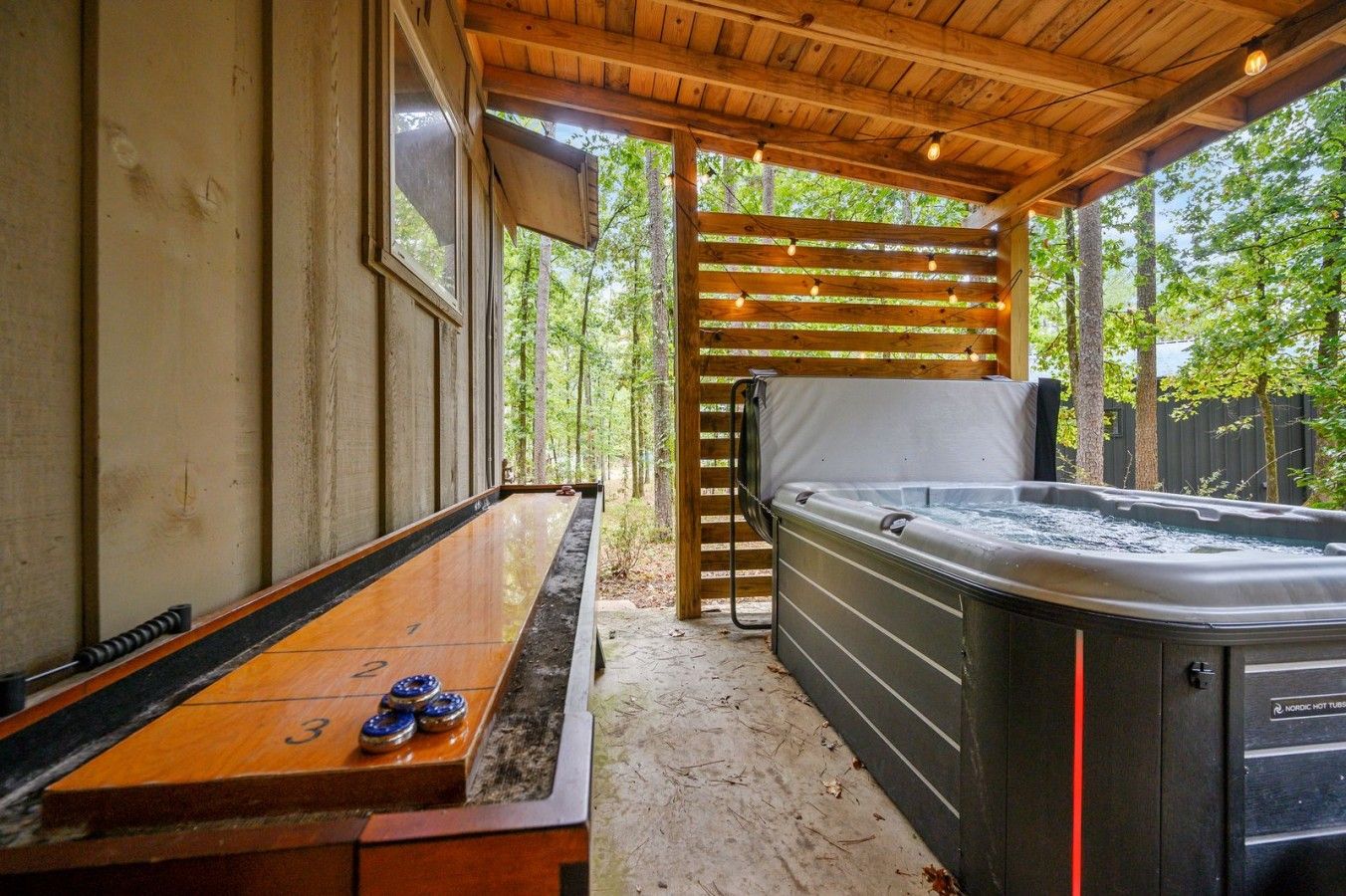 Un jacuzzi bajo una pérgola de madera con una mesa de juego de bolos cerca.