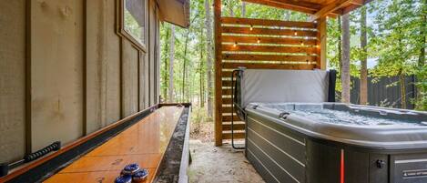 Un jacuzzi bajo una pérgola de madera con una mesa de juego de bolos cerca.